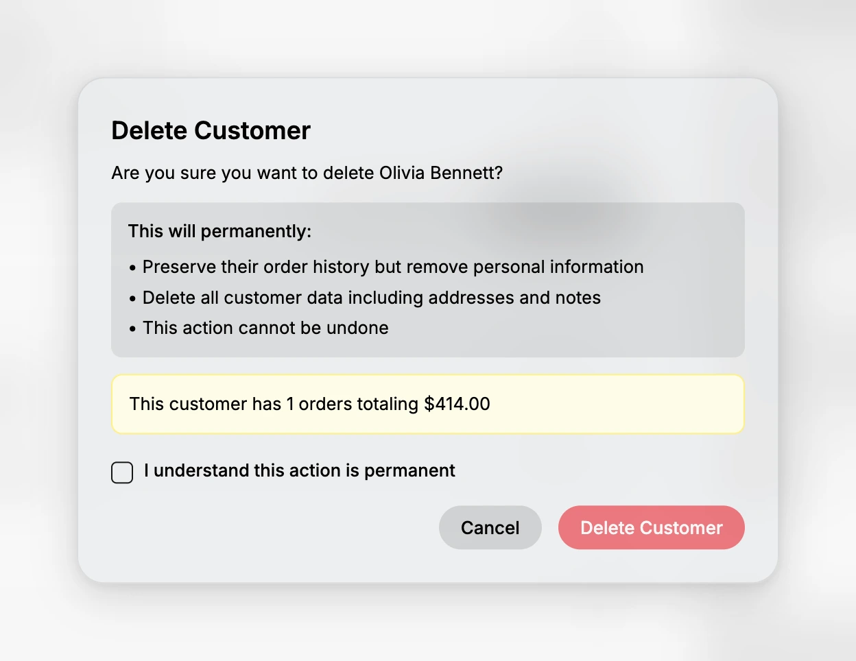 The Delete Customer dialog over the blurred page behind it. It asks whether you are sure you want to delete Olivia Bennett, then lists that it will preserve their order history but remove personal information, delete all customer data including addresses and notes, and that this action cannot be undone. A highlighted note gives her order count and total. Below it sits an unticked checkbox reading I understand this action is permanent, with Cancel and a faded Delete Customer button.